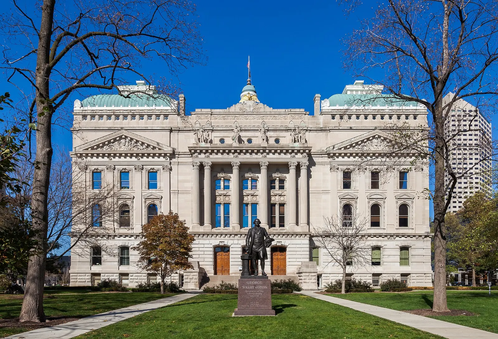 Indiana Statehouse in Indianapolis, a limestone building with a central colonnade and green copper domes, with a bronze statue on the lawn in front