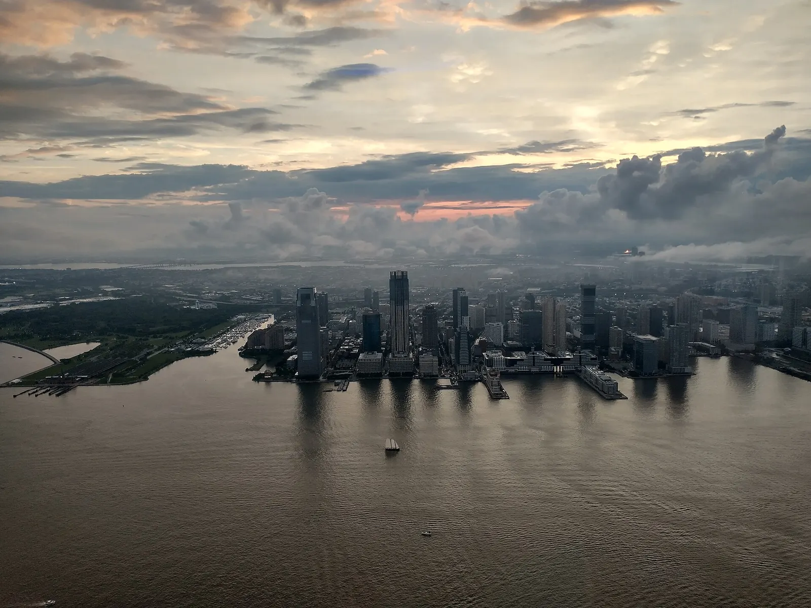 Aerial view of the Jersey City waterfront towers on the Hudson River under a cloudy sunset sky