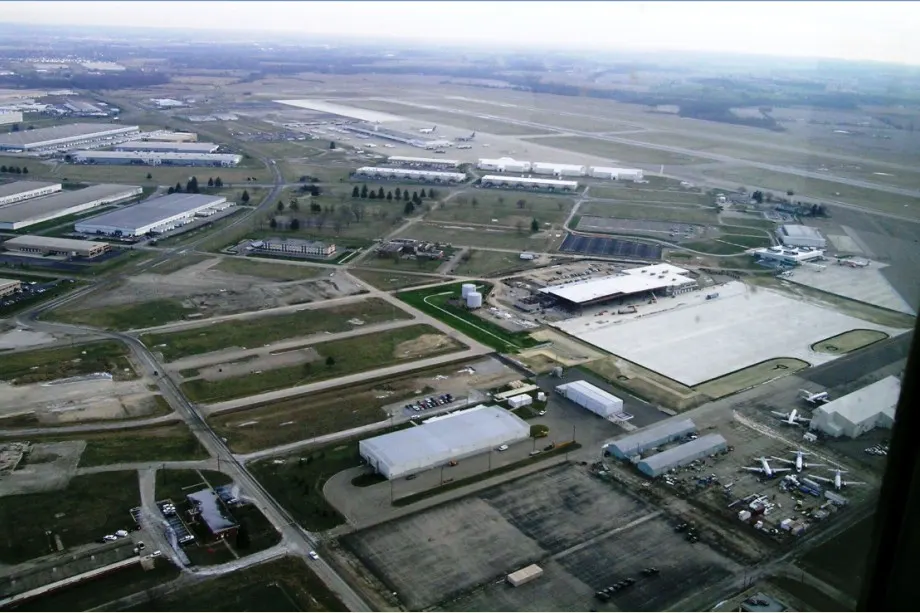 Aerial view of Rickenbacker International Airport in Ohio on a hazy day, with warehouse buildings, a large concrete apron and aircraft parked near the runways