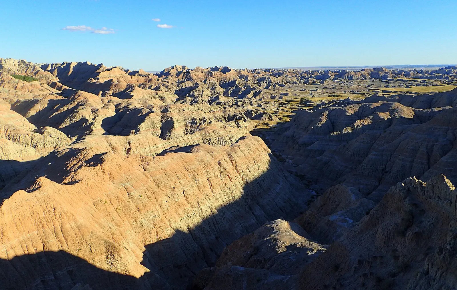 Eroded ridges and canyons of Badlands National Park in South Dakota, lit by low sun with long shadows under a clear blue sky