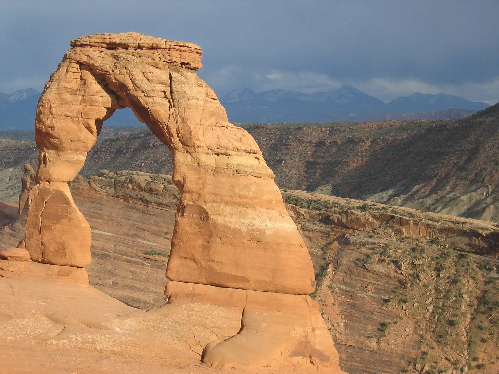Delicate Arch, a freestanding red sandstone arch in Arches National Park, Utah, with distant mountains under a stormy sky